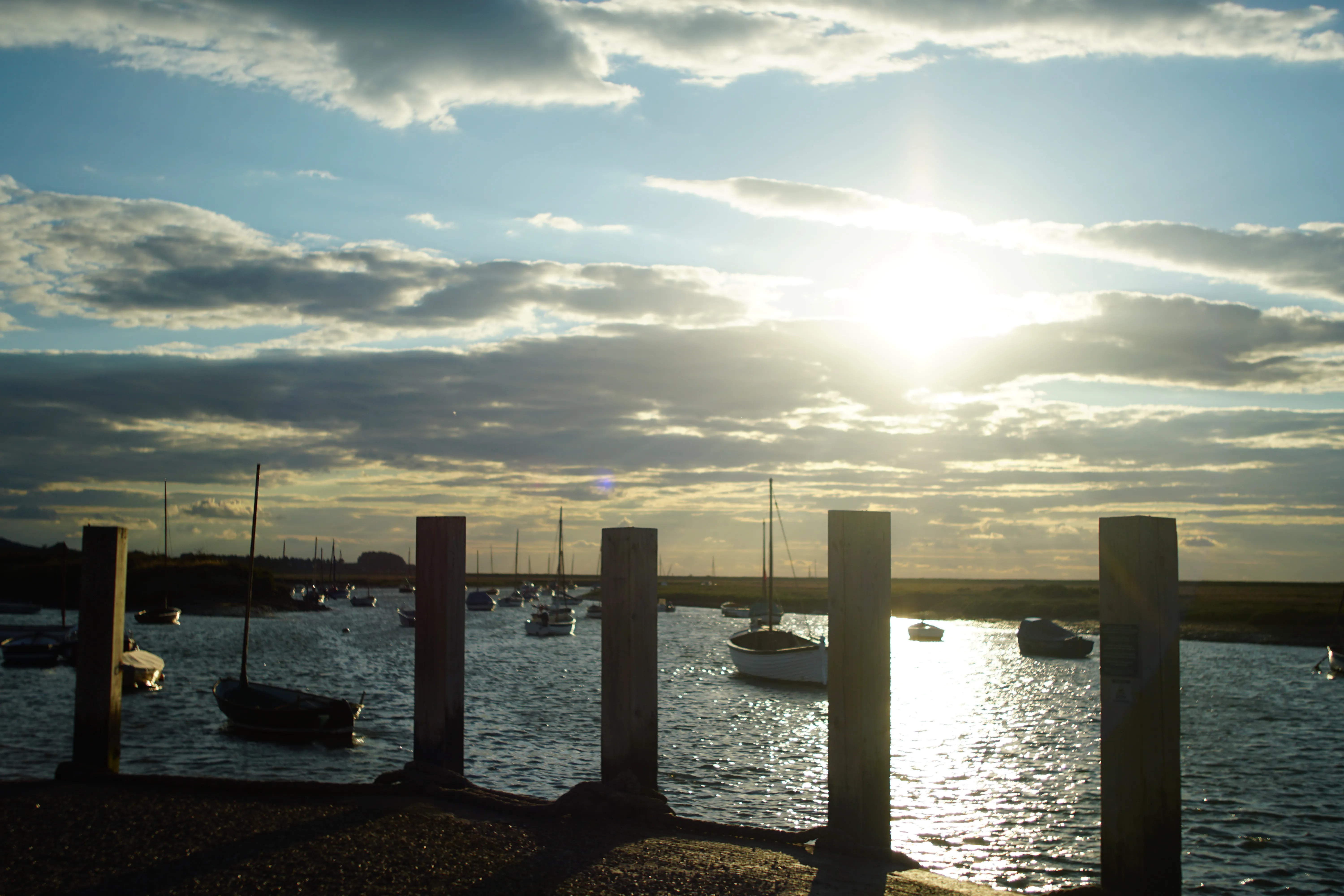 Burnham Overy Staithe when the tide is high, with the creek full between the mooring posts at the head of the quay and boats afloat under a low evening sun.