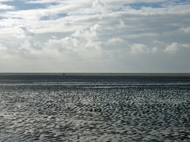 The Wash at low water off Hunstanton, an immense flat of rippled wet sand reaching to the horizon, with two tiny distant figures giving the only sense of scale.